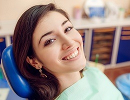 Smiling woman in dental chair after porcelain veneer treatment