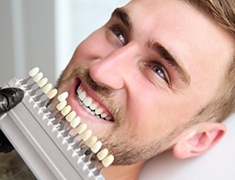 Man's smile compared with tooth color chart after teeth whitening