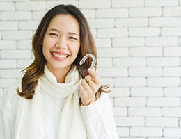 Smiling woman in white holding her Invisalign