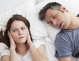 Woman covering ears next to snoring man in need of sleep apnea therapy