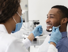 A younger man smiling at his dentist while she prepares to examine his oral cavity during a checkup