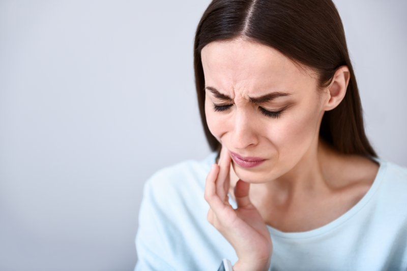 Woman rubbing jaw due to TMJ pain in Ann Arbor