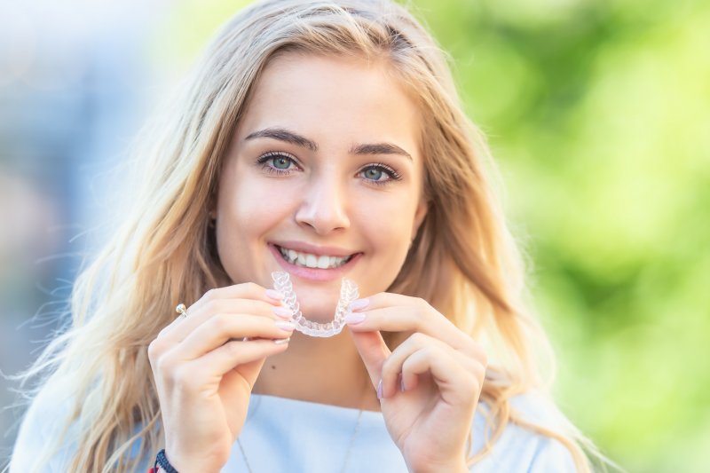 person holding Invisalign aligner tray and smiling