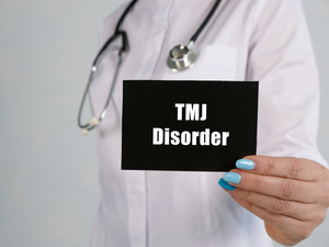 Dentist holding up a little black card that says “TMJ disorder”